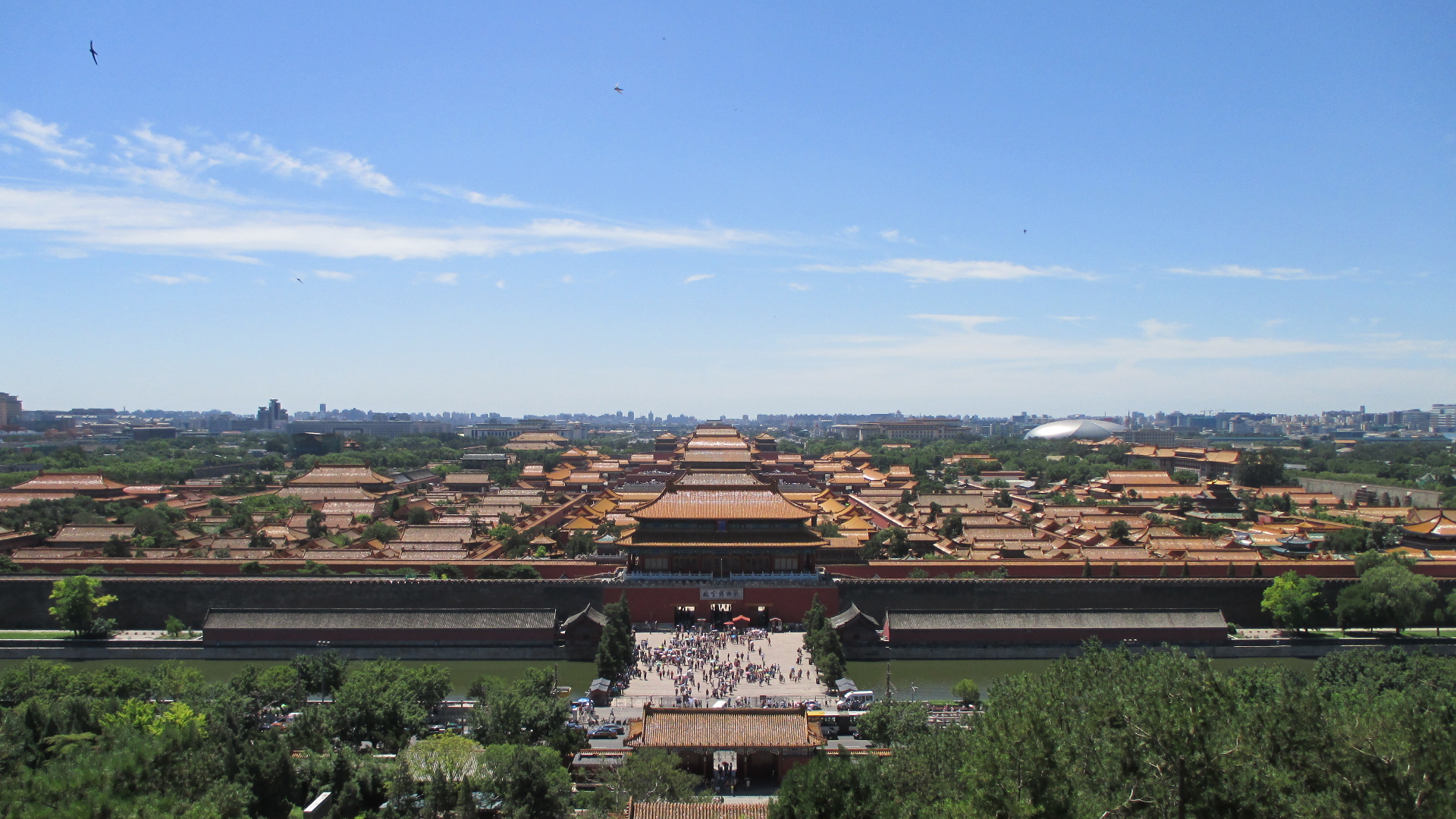 The Forbidden City seen from Jingshan Park on a clear July day, with summer greenery and visitors below.