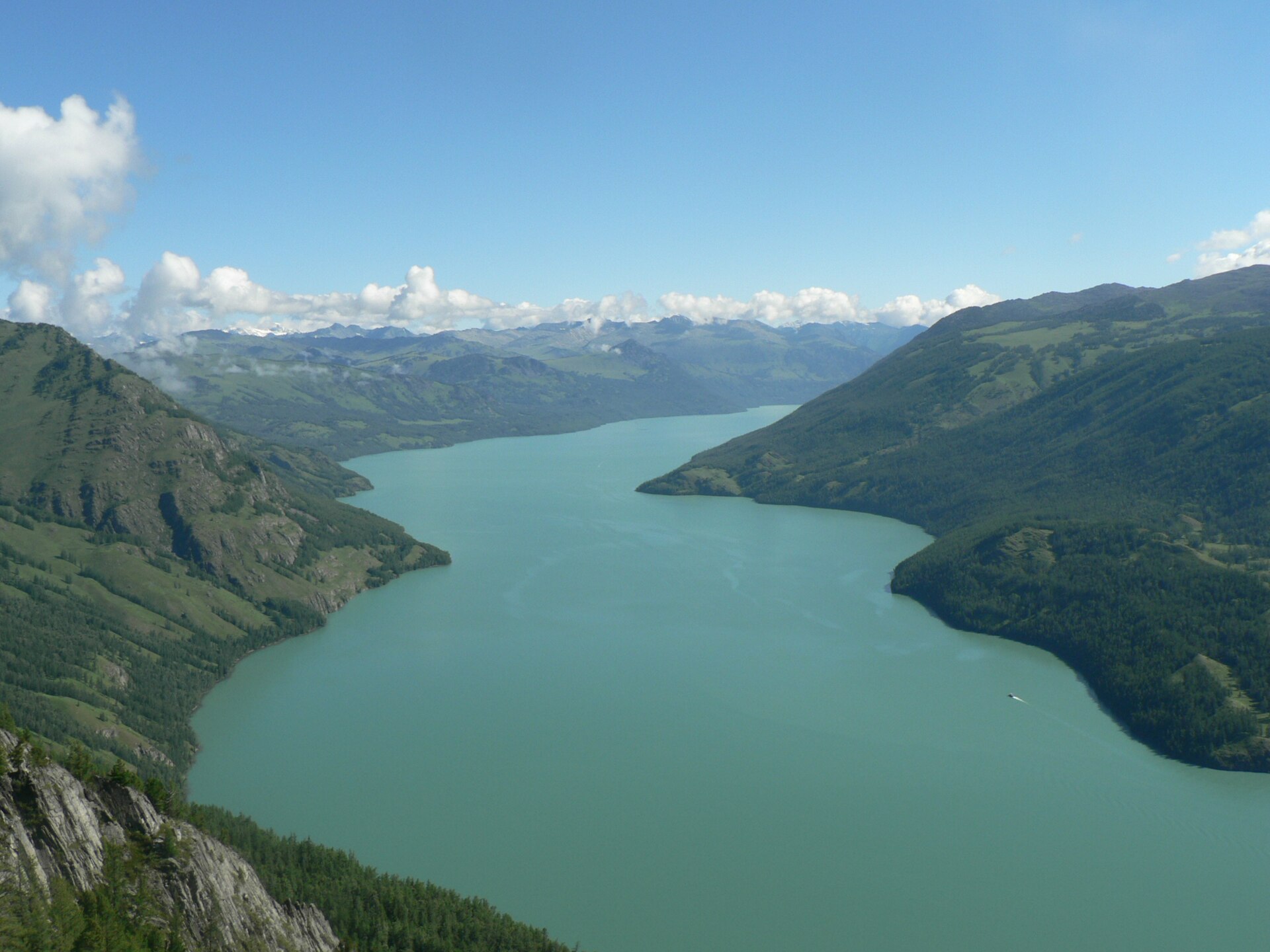Kanas Lake stretches between forested mountain slopes under a blue sky in July 2005.